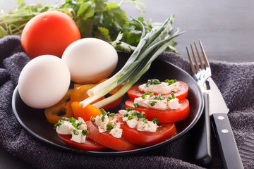 Sliced tomatoes with cheese and herbs in a black plate with onions, sweet peppers and eggs. Close-up