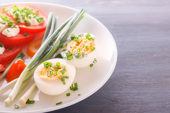 Half boiled eggs with tomatoes, green onions sprinkled with greens in a white plate on a gray wooden table. Close-up