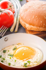 Fried egg in a pan, sliced bread, tomatoes and green onions are cooked for breakfast on a wooden gray table. Close-up