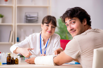 Fototapeta premium Young man with bandaged arm visiting female doctor traumatologis