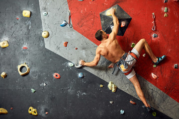 Sporty strong young man with tanned muscular naled torso exercising in boulder climbing hall...