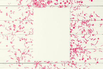 Empty white sheet with festive confetti on a white wooden background, top view