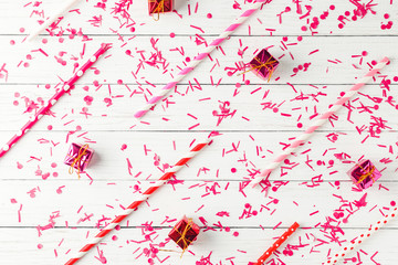 Pattern of confetti, tubes for drinking and small gifts on a white background, top view, flat lay