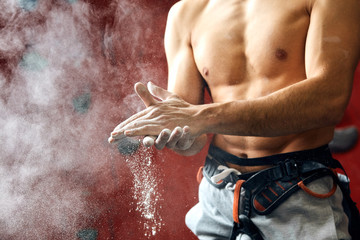 Closeup of muscular male with perfect shaped body coating his hands in powder chalk magnesium preparing to climb, motion shot of chalk. Close-up photo of a climber putting talc on his palms