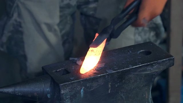 Forge hot metal Making the knife out of metal at the forge. Close up blacksmith's hands hitting hot metal with a massive hammer on an anvil.