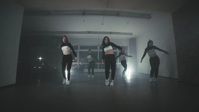 Group of young hip-hop dancers performing on the stage. Happy dancing women. Girls enjoying funky hip hop moves in dark studio with smoke and lighting. Wide angle