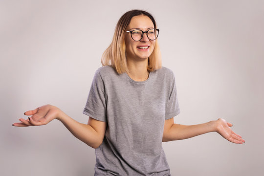 I don't know concept. Young laughs woman who do not understand what is happening. The girl in big eyeglasses and gray shirt raises hands and shrugging shoulders on a gray background copy spac