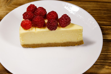 Piece of tasty New York cheesecake with raspberries in a white plate on wooden table
