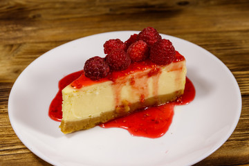 Piece of tasty New York cheesecake with raspberries and raspberry jam in a white plate on wooden table