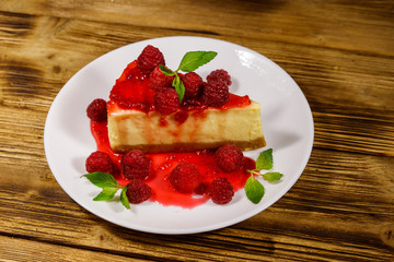 Piece of tasty New York cheesecake with raspberries and raspberry jam in a white plate on wooden table