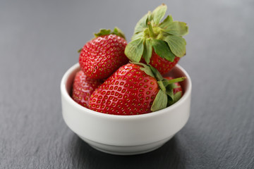 ripe strawberries in white bowl on slate background