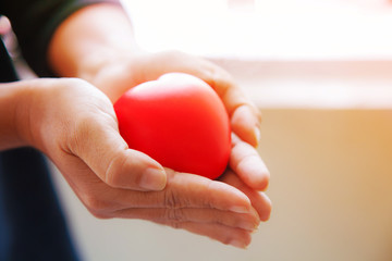 red heart in female's both hands in black suit background, represents helping hands in hard time, caring, love, sympathy, condolence, patient assistance, life moment, psychological support concept