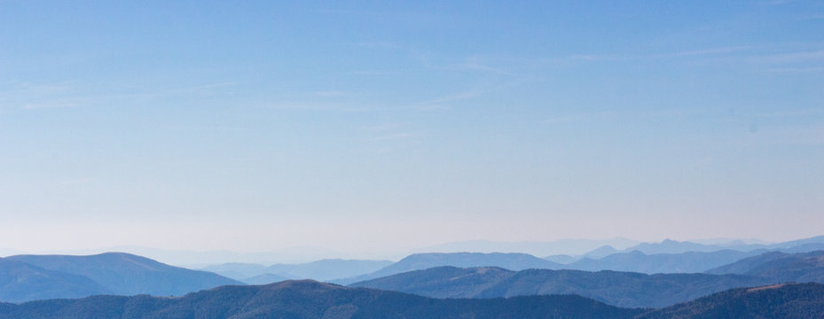 Blue mountains peaks panorama. Vastness and calmness concept. Clear blue sky over blue mountains on sunset. Mystical aerial panorama. Misty silhouettes of Carpathian mountains. Travel and tourism.