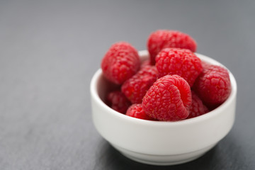 ripe raspberries in white bowl on slate background