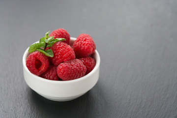 ripe raspberries in white bowl on slate background