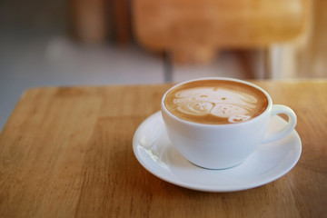 Hot coffee latte cup with cute pug dog latte art milk foam on light wood table with morning sunlight in relaxing coffee shop background.