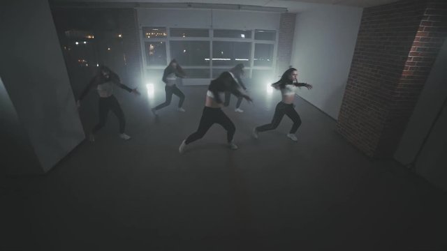 Group of young hip-hop dancers performing on the stage. Girls enjoying funky hip hop moves in dark studio with smoke and lighting. Happy dancing women. Wide angle