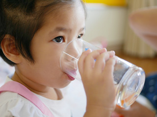 Little Asian baby girl, 34 months old, drinking water from a glass / cup by herself