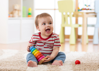 Baby toddler boy playing with developmental toy sitting on soft carpet at home