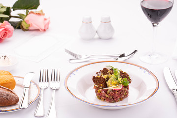 Giving of a dish the Tartar from beef with capers and grated cheese with vegetables and greens