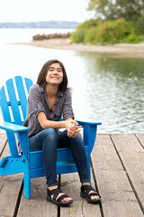 Biracial teen girl relaxing on blue adirondak chair by lake