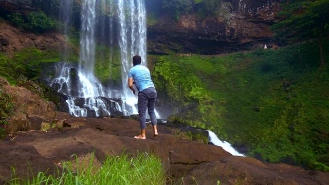 strong man climbs up rock watches waterfall streams