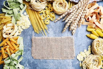 Mixed types and shapes of italian pasta on grey stone, background
