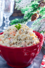 Traditional Russian New Year's salad in a red bowl with New Year's decor, selective focus
