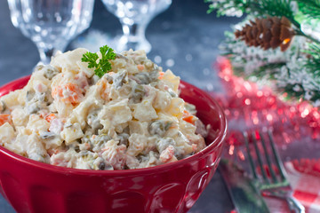 Traditional Russian New Year's salad in a red bowl with New Year's decor, horizontal, copy space