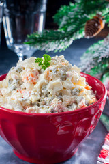 Traditional Russian New Year's salad in a red bowl with New Year's decor, selective focus
