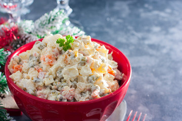 Traditional Russian New Year's salad in a red bowl with New Year's decor, horizontal, copy space