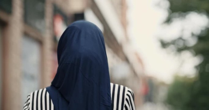 Attractive muslim girl wearing hijab walking down the street, talking with someone on phone, twirling around and looking at camera - modern muslim, modern lifestyle concept closeup 4k