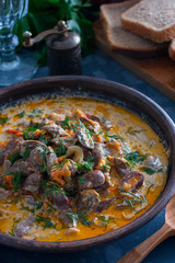 Chicken hearts stewed in sour cream in a clay bowl, selective focus