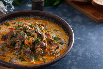 Chicken hearts stewed in sour cream in a clay bowl on a wooden stand, horizontal