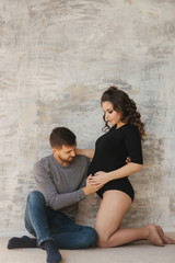 Happy man put his handr on the belly of his pregnant wife. Young family in studio. Couple wait for a baby