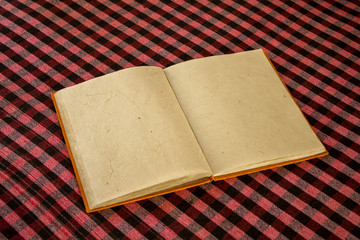 an open orange book with blank sheets of natural rough paper lies on the checkered tablecloth of the table. white red black cell