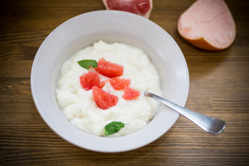 sweet boiled semolina porridge in a plate with slices of red grapefruit