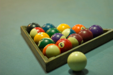 multicolored blurred billiard balls with numbers lie in a wooden triangle pyramid on the blue cloth of the table