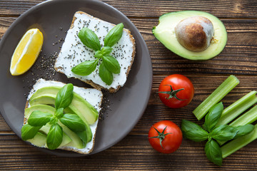 Tasty avocado sandwiches with cream cheese, quinoa seeds and cheery tomatoes on brown background.