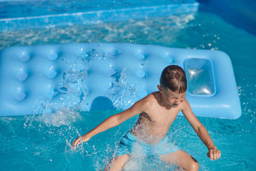 Boy having fun in swimming pool at hotel. He making jump from inflatable mattress into water.