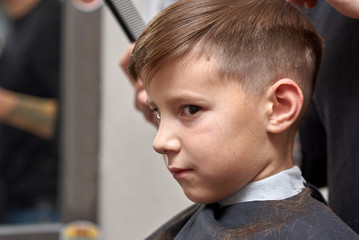 Boy  getting hairstyle in barbershop in London.