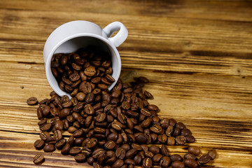 Roasted coffee beans spill out of cup on wooden table