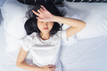 Naklejka premium Woman stretching in bed after waking up, back view. Woman sitting near the big white window while stretching on bed after waking up with sunrise at morning, back view.