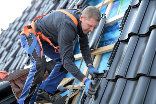 Dachdecker Arbeiter auf Dachlatten stehend am Gurt beim Hausbau auf einer Immobilie, Reparatur und Dachdecker Arbeiten auf Baustellen mit erh&ouml;hter Arbeitssicherheit durch pers&ouml;nliche Schutzausr&uuml;stung