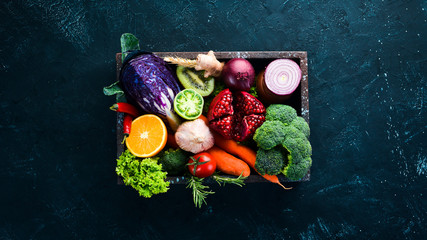 Fototapeta na wymiar Fresh vegetables and fruits in a wooden box on a black background. Organic food. Top view. Free copy space.