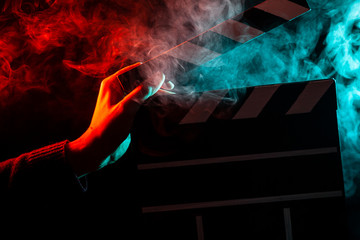 Close-up on an open clapper in hand before starting shooting a film with multi-colored smoke around...