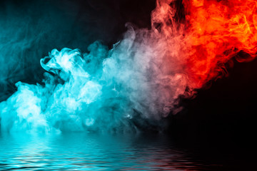 A column of colored smoke of blue and red color from a wap of an abstract form tending upwards on a black isolated background above a river with small waves.