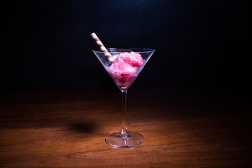 Martini glass filled with colorful fruit ice cream on dark background with toned light and fog