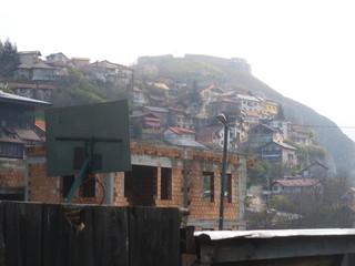 A bare brickwork house in Sarajevo. In the background is a hill with houses.