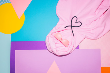 Fashion woman's pink hoodie with black laces in shape of heart and sunglasses on memphis style background. Geometry minimal concept. Fall and winter.
